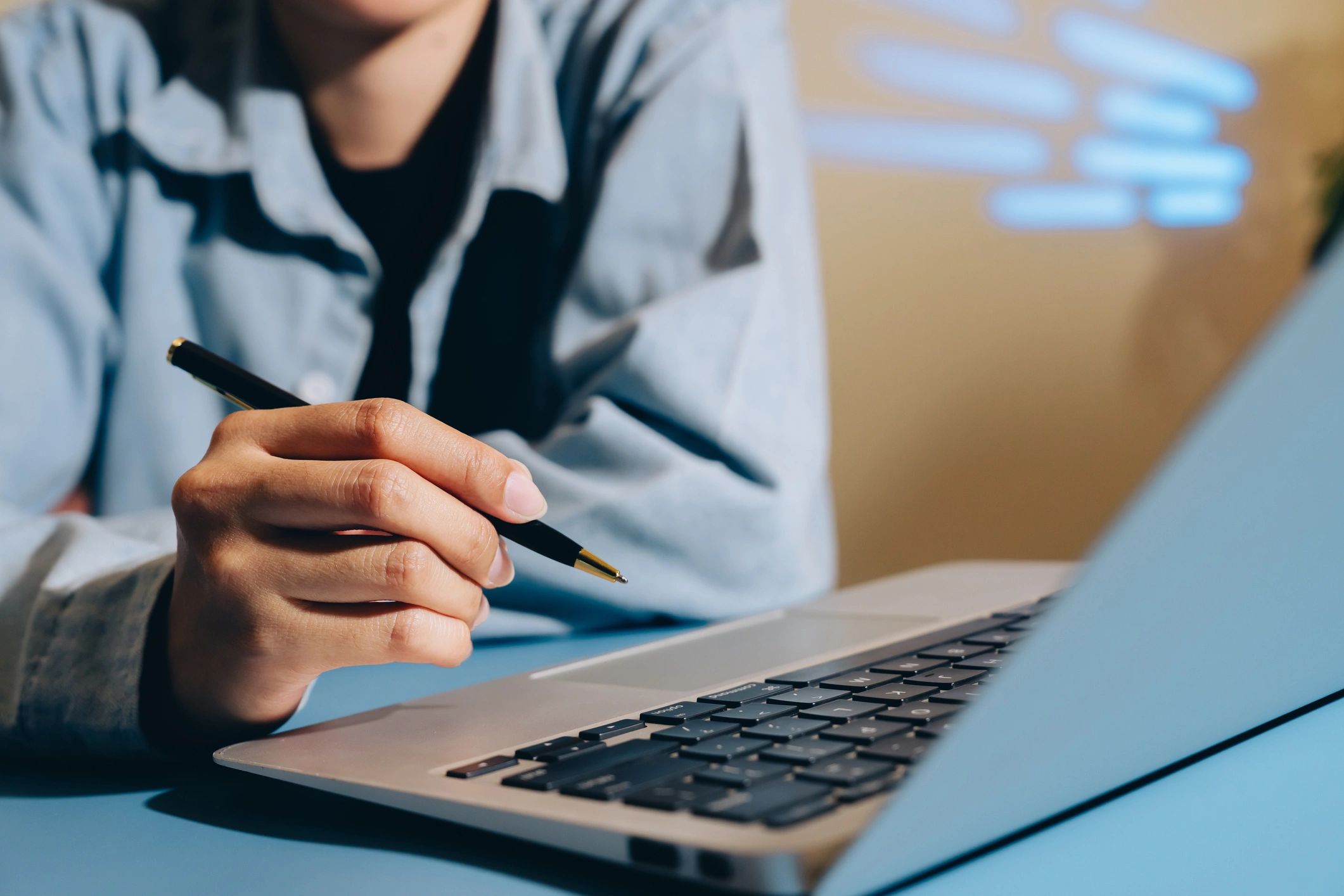 Person working on laptop with pen, focused workspace